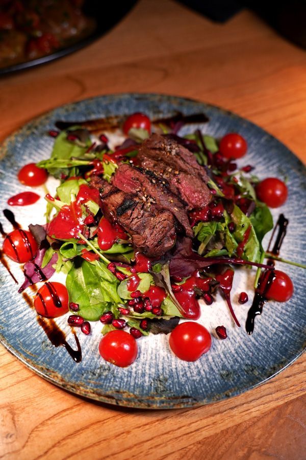 Gegrillter Steaksalat auf einem blauen Teller, garniert mit Salat, Kirschtomaten und Balsamico-Dressing