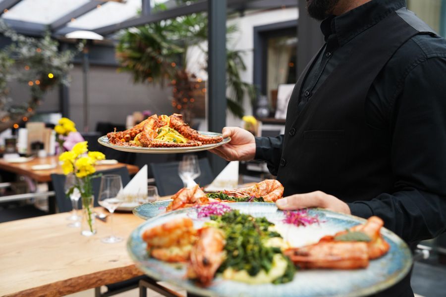 Kellner trägt angerichtete Meeresfrüchtegerichte auf der Terrasse eines Restaurants.