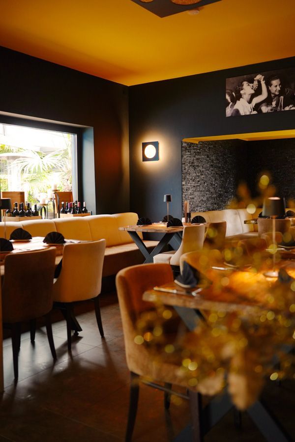 Warmes, dezent beleuchtetes Restaurantinterieur mit gelber Decke, dunklen Wänden und zum Essen gedeckten Tischen.