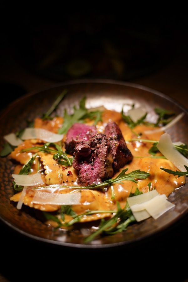 Gourmet-Tellergericht mit angebratenem Fleisch, cremiger Sauce, Gemüse und gehobeltem Käse in einer dunklen Schüssel