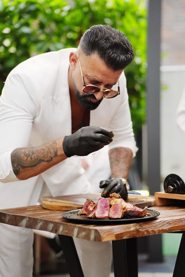 Ein Koch in weißer Kochjacke richtet ein Gourmet-Steak an einem Tisch im Freien an.