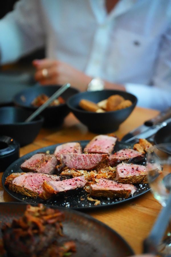 Gegrilltes, in Scheiben geschnittenes Steak auf einer schwarzen Platte mit Beilagen an einem Restauranttisch