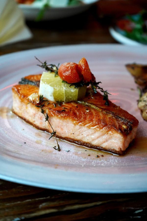 Gebratenes Lachsfilet mit Kräuterbutter auf einem rosa Teller, garniert mit Kirschtomaten und Thymian.