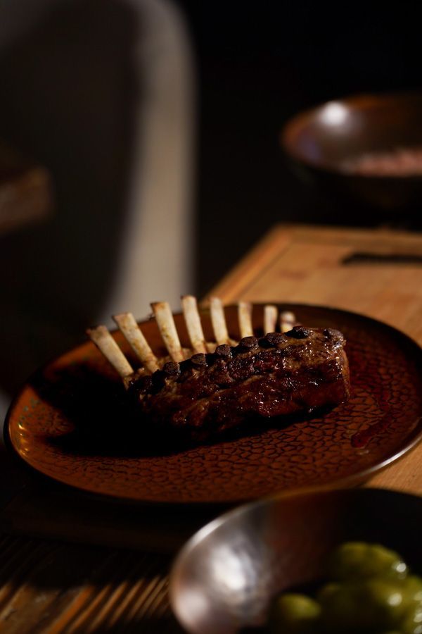 Ein auf einem dunklen Tisch angerichtetes Steak mit Rippenknochen steht neben einer Metallschale mit grünen Trauben.