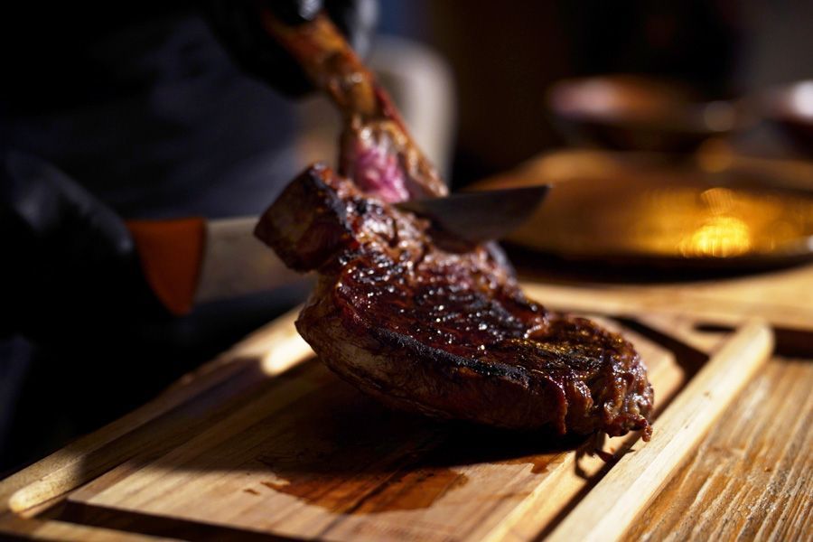 Gegrilltes Steak wird auf einem Holzbrett im warmen Restaurantlicht aufgeschnitten.