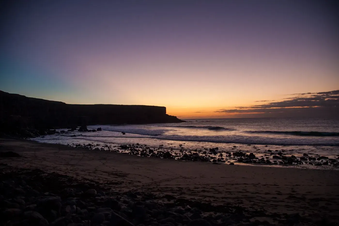 Una puesta de sol sobre una playa con un acantilado al fondo