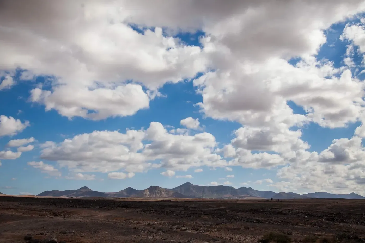 Un paisaje desértico con montañas al fondo y nubes en el cielo.