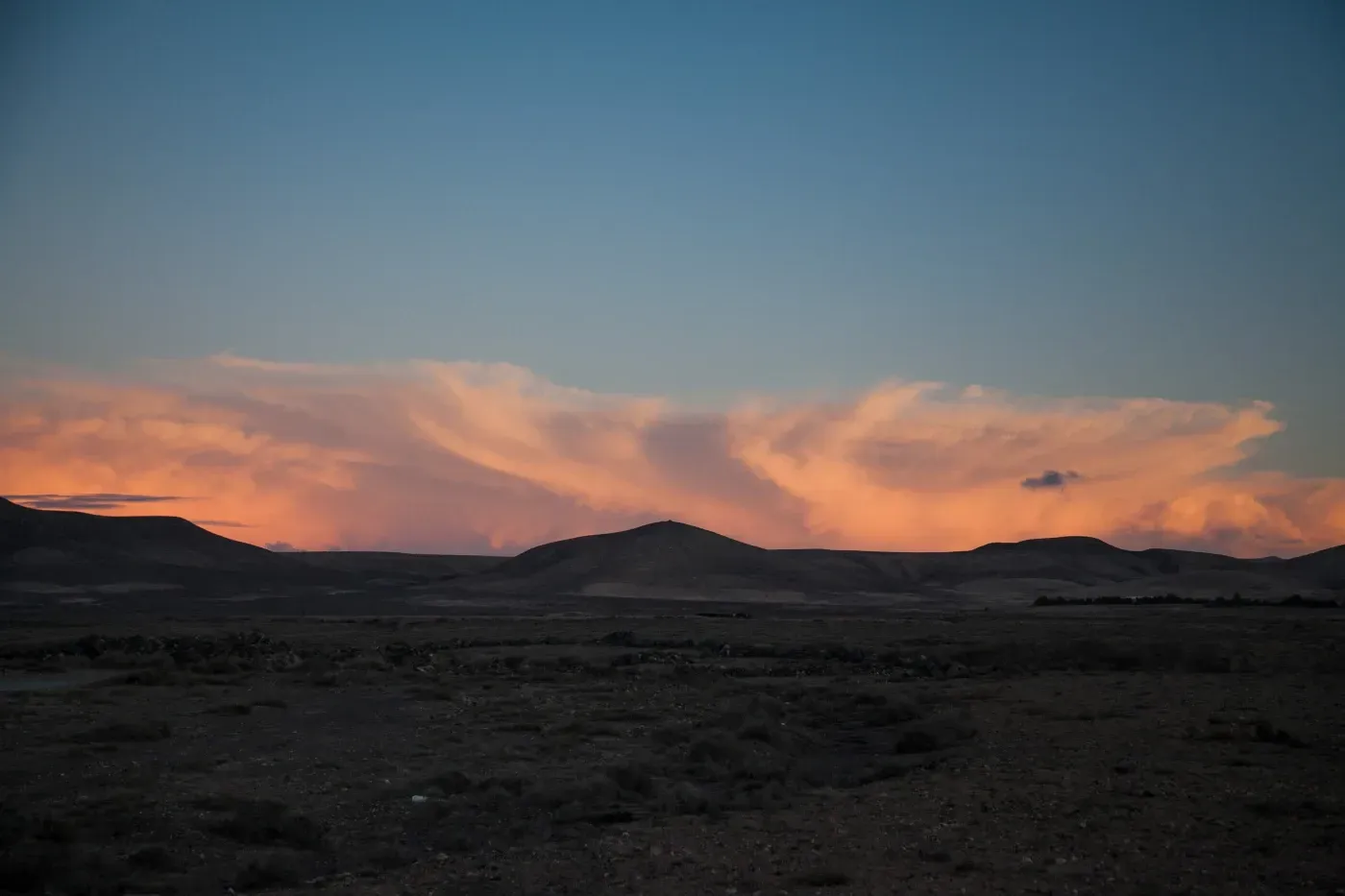 Una puesta de sol sobre un desierto con montañas al fondo