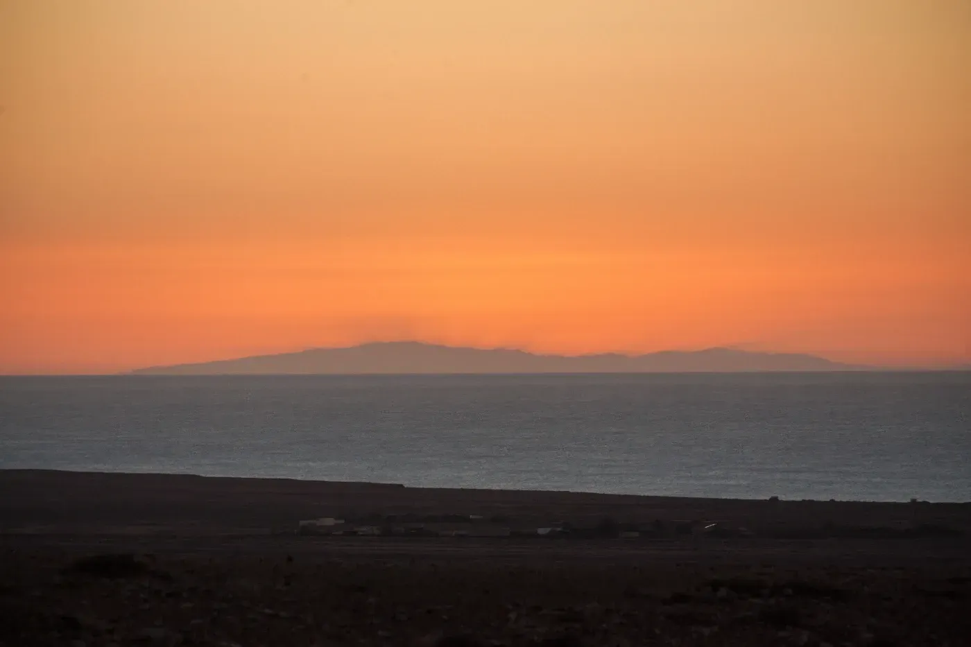 Una puesta de sol sobre el océano con montañas en la distancia.