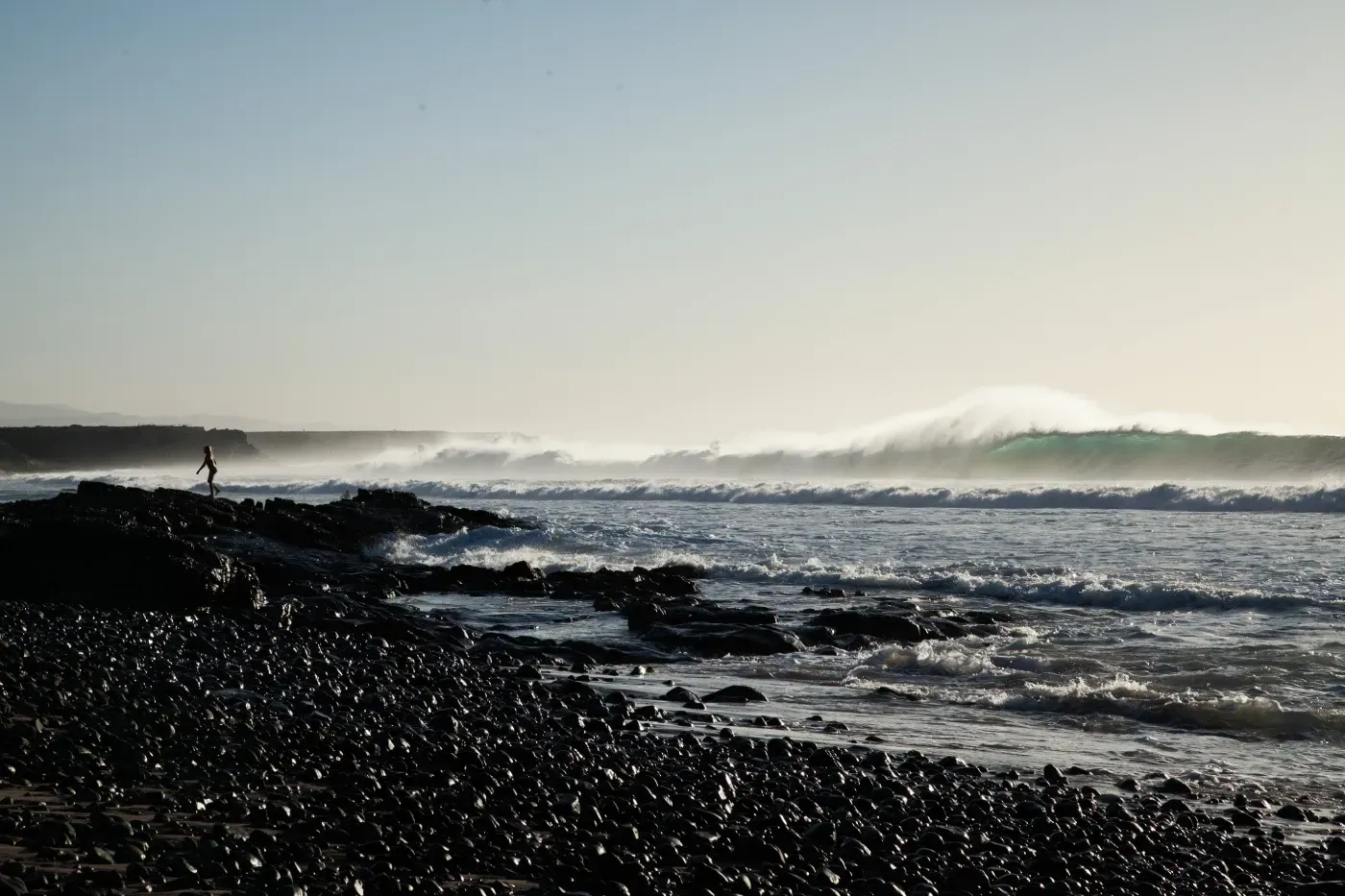 Una persona está parada en una playa rocosa cerca del océano.