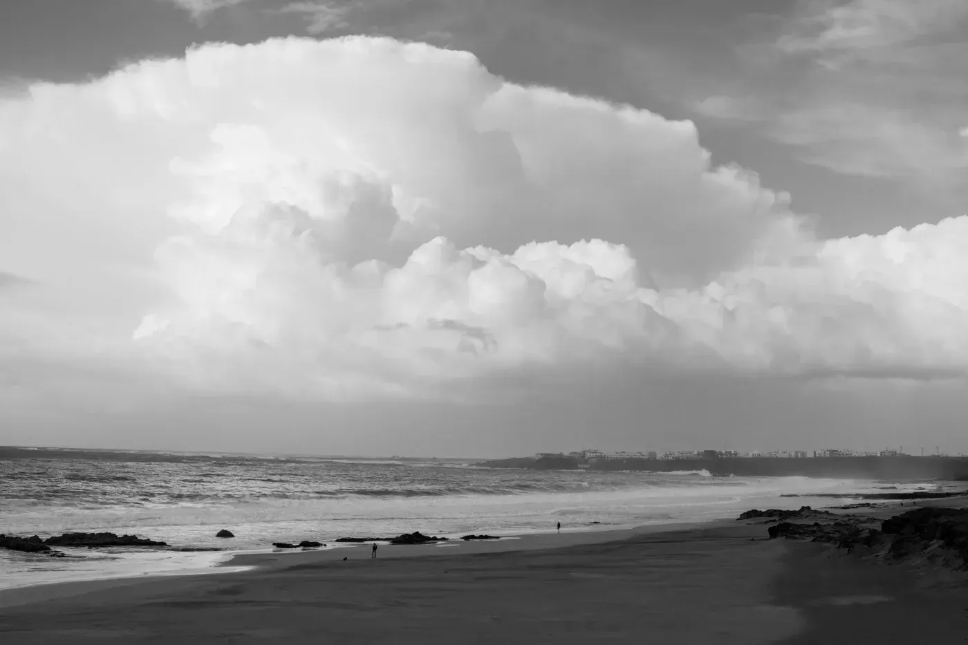 Una fotografía en blanco y negro de una playa con una gran nube en el cielo.