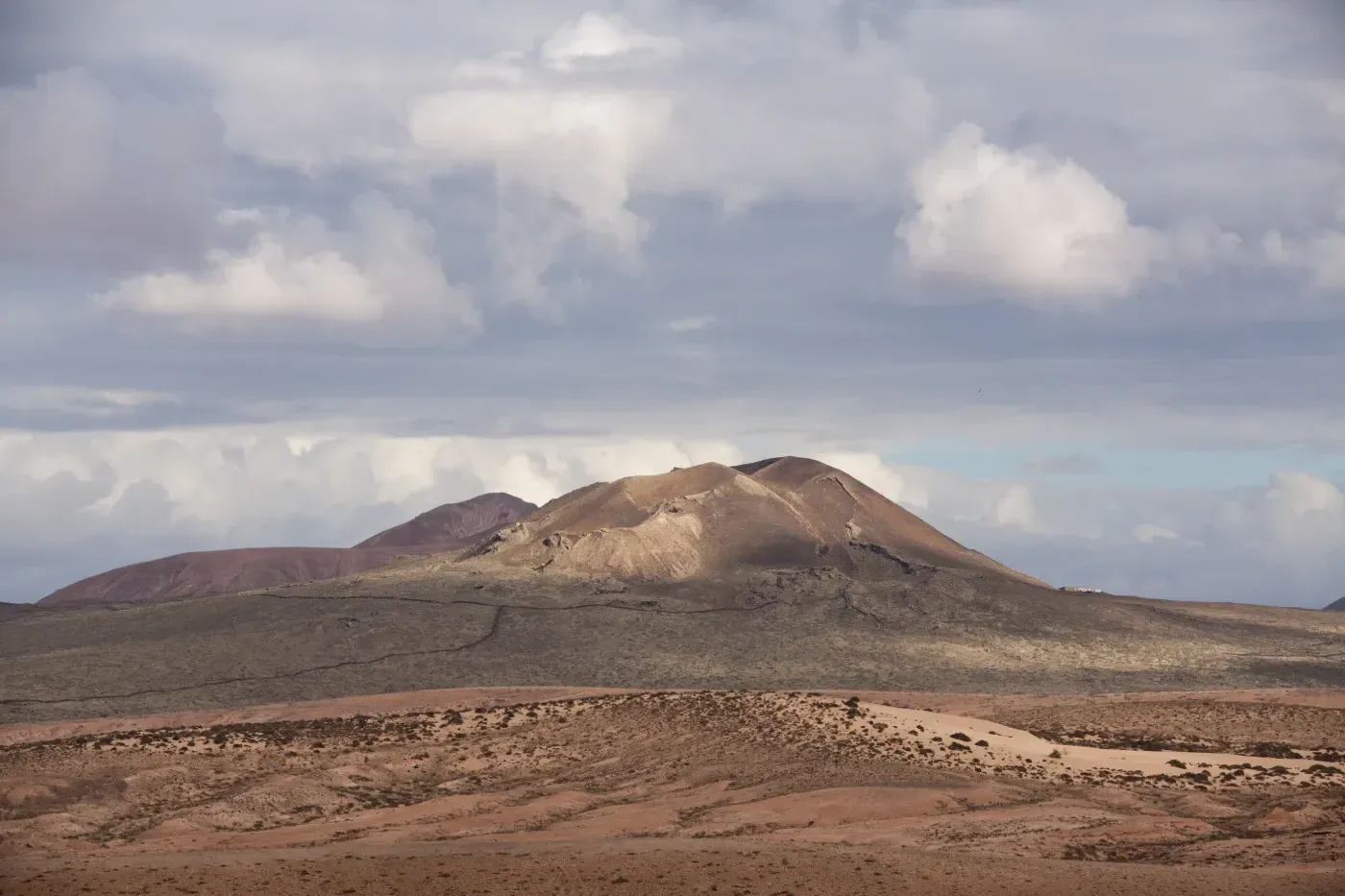 Un paisaje desértico con una montaña al fondo y nubes en el cielo.