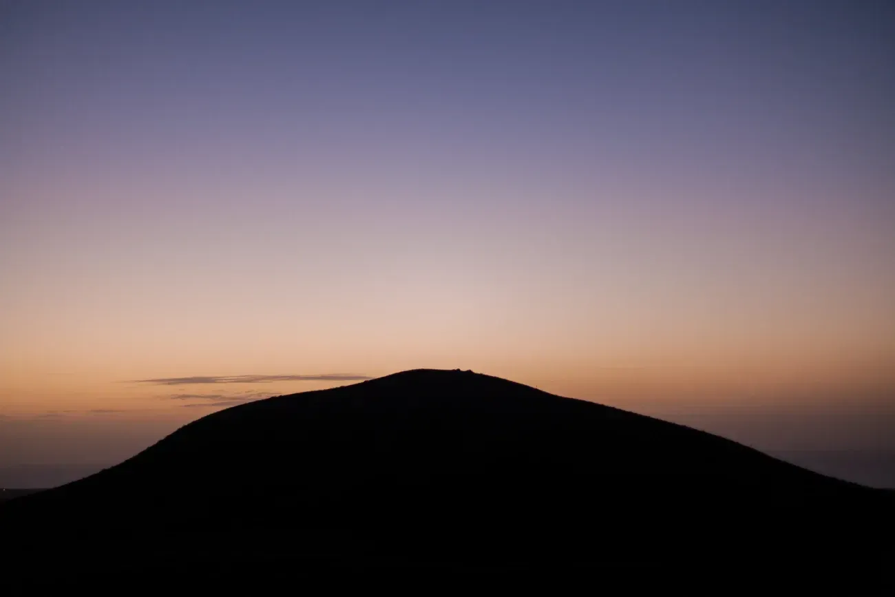 Una silueta de una montaña al atardecer con un cielo púrpura en el fondo.