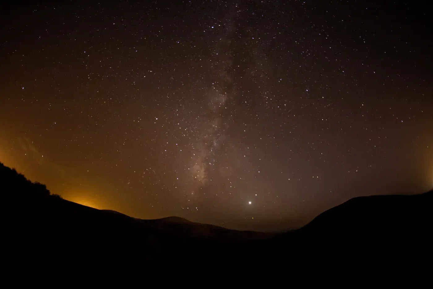 Un cielo nocturno lleno de muchas estrellas y montañas en primer plano.