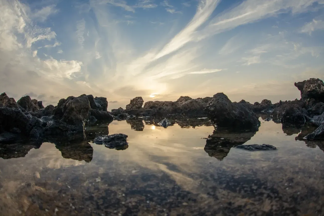 El sol se está poniendo sobre un cuerpo de agua rodeado de rocas.