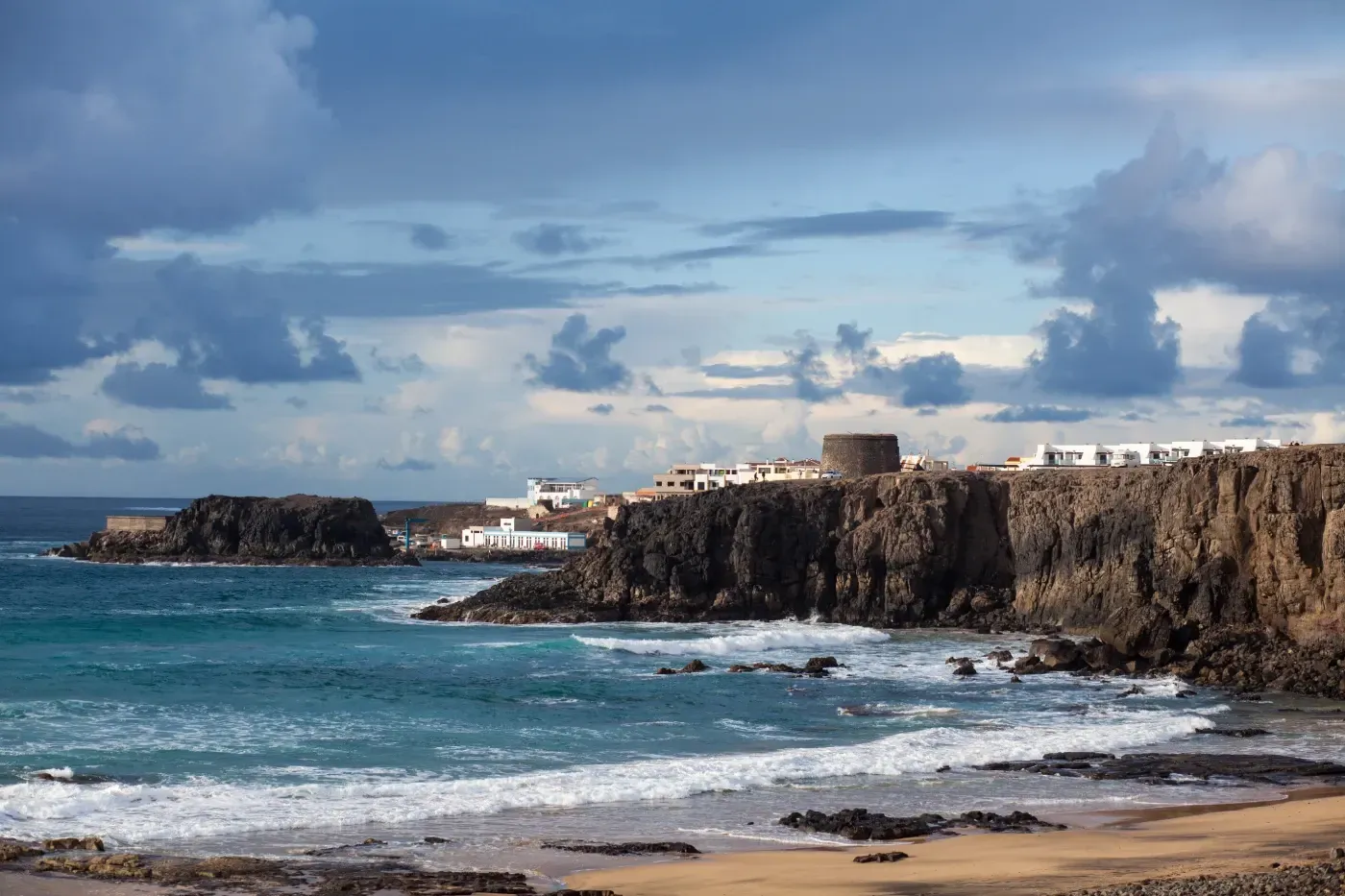 Un acantilado con vistas al océano con olas rompiendo en la orilla.