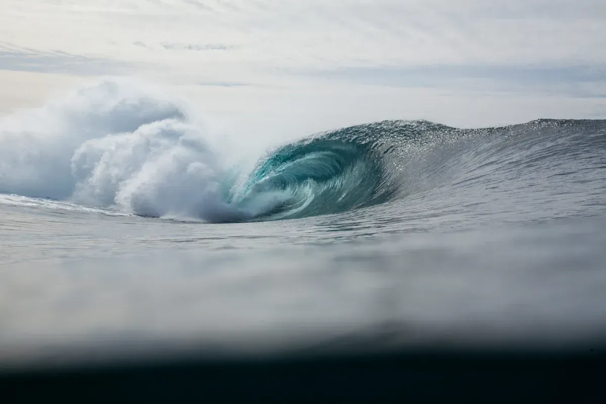 Una gran ola rompe en el océano en un día nublado.