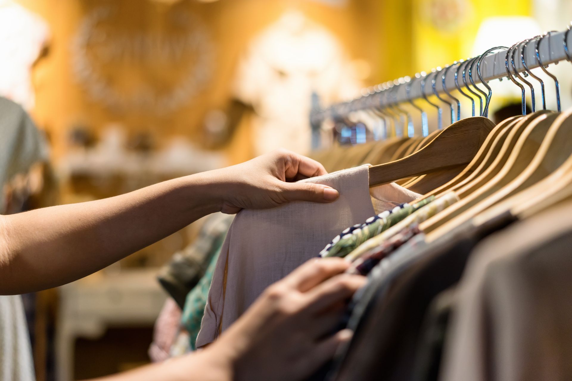 Des mains parcourent des vêtements sur des cintres dans un rayon de magasin.