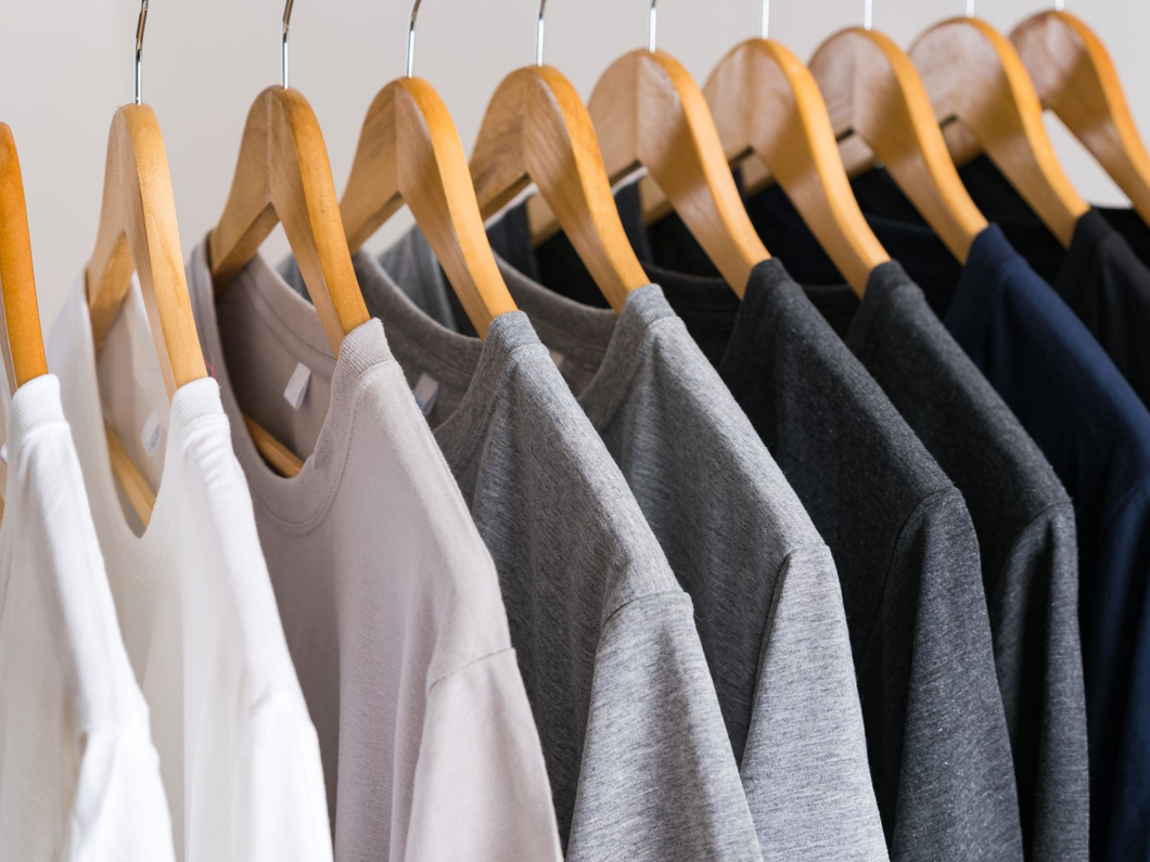 Des vêtements sur des cintres en bois, notamment des chemises blanches, grises et foncées, suspendus à un portant.
