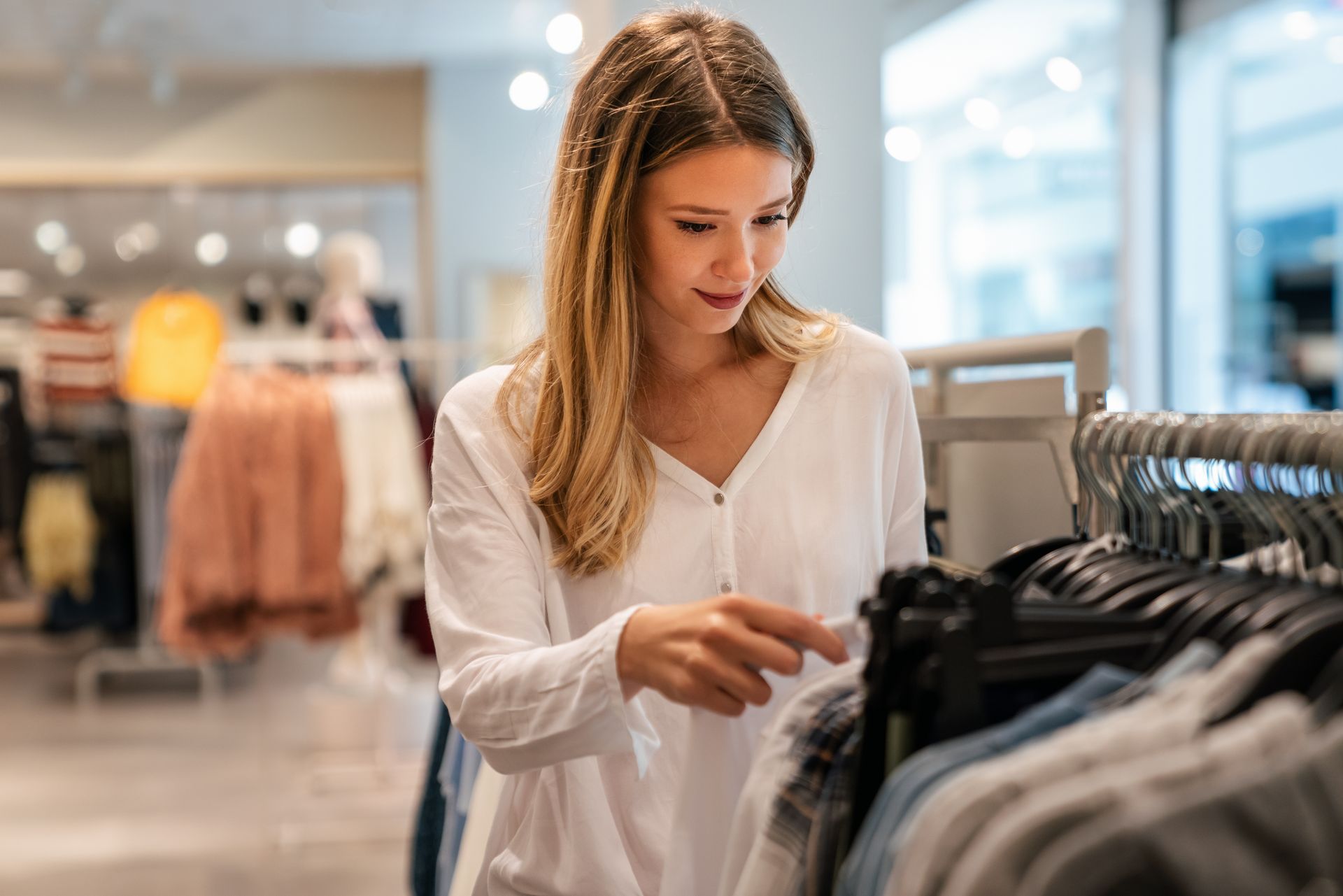 Une femme regarde des vêtements sur un portant dans un magasin de vêtements lumineux.