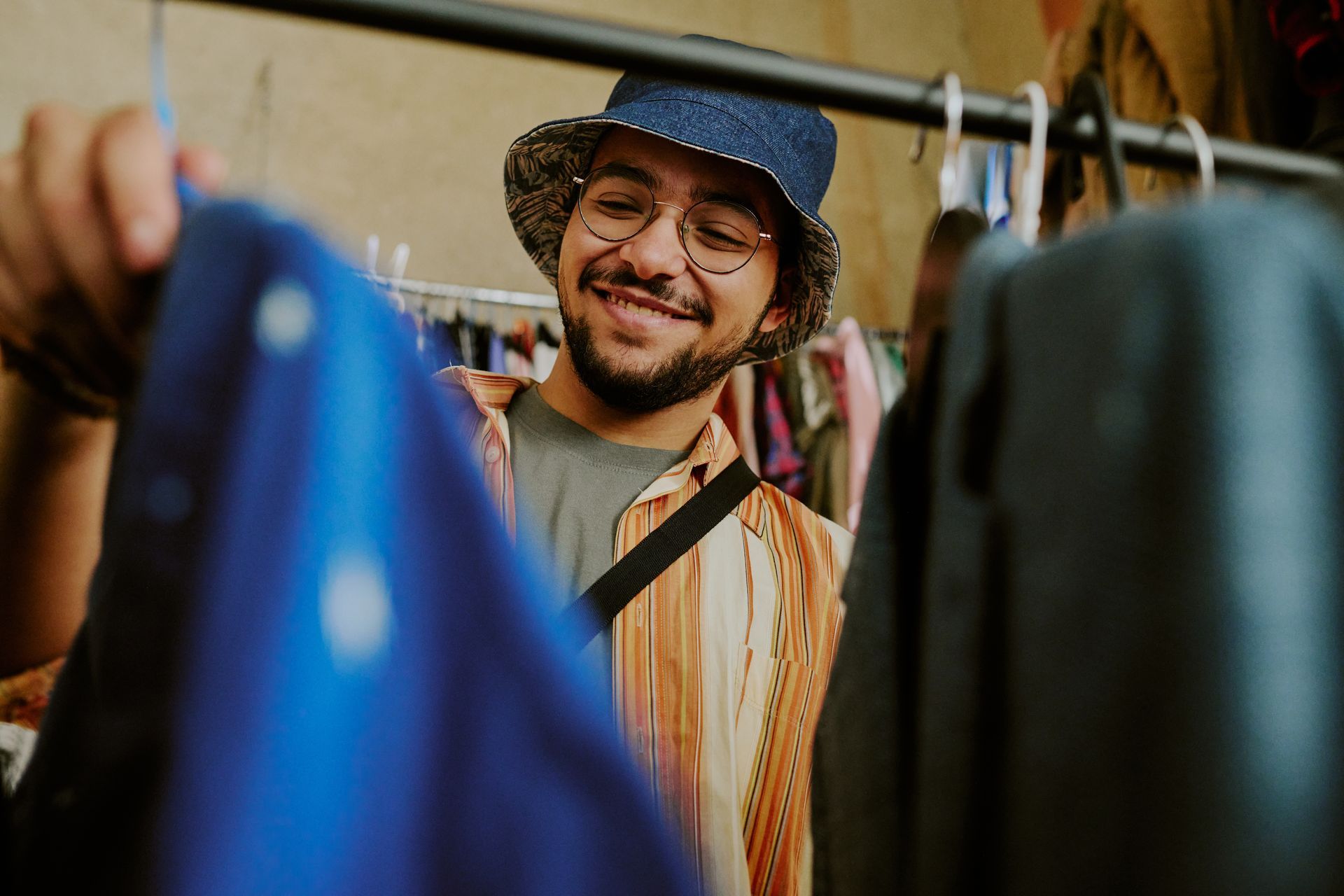 Une personne souriante portant un chapeau regarde des vêtements sur un portant dans un magasin