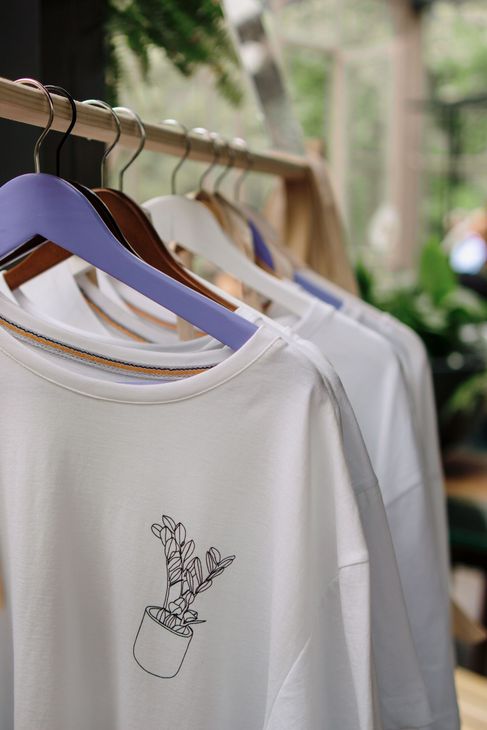 Des t-shirts blancs sur des cintres en bois, suspendus à un portant à vêtements à l'extérieur.