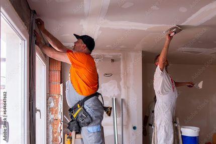 Deux ouvriers appliquent de l'enduit à plaques de plâtre sur un plafond lors de la rénovation d'une maison.