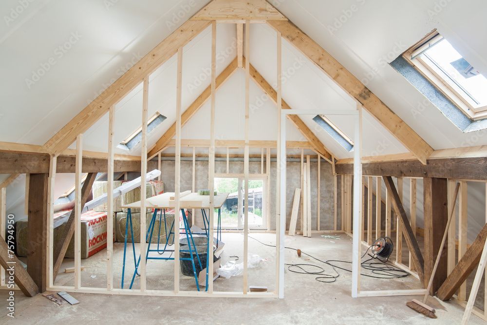 Grenier non aménagé avec charpente en bois apparente, puits de lumière et outils de construction à l'intérieur.