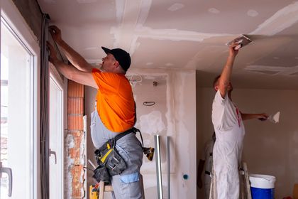 Deux ouvriers appliquent de l'enduit à plaques de plâtre sur un plafond lors de la rénovation d'une maison.