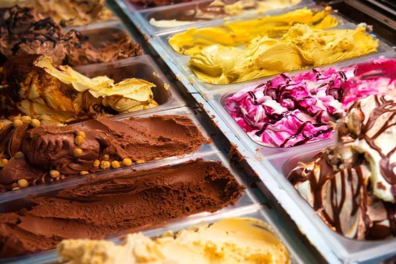 Surtido de sabores de helado en una vitrina, incluyendo chocolate, amarillo, rosa y remolinos de vainilla.