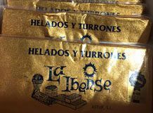 Envoltorios de caramelos dorados apilados con la etiqueta “HELADOS Y TURRONES” y un logotipo parcialmente visible.