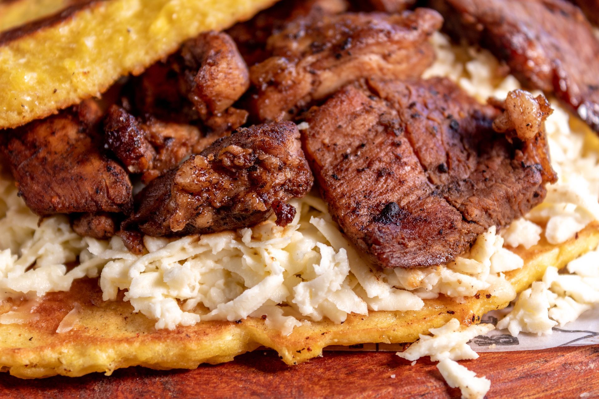 Un primer plano de un sándwich con carne y queso en una mesa de madera.