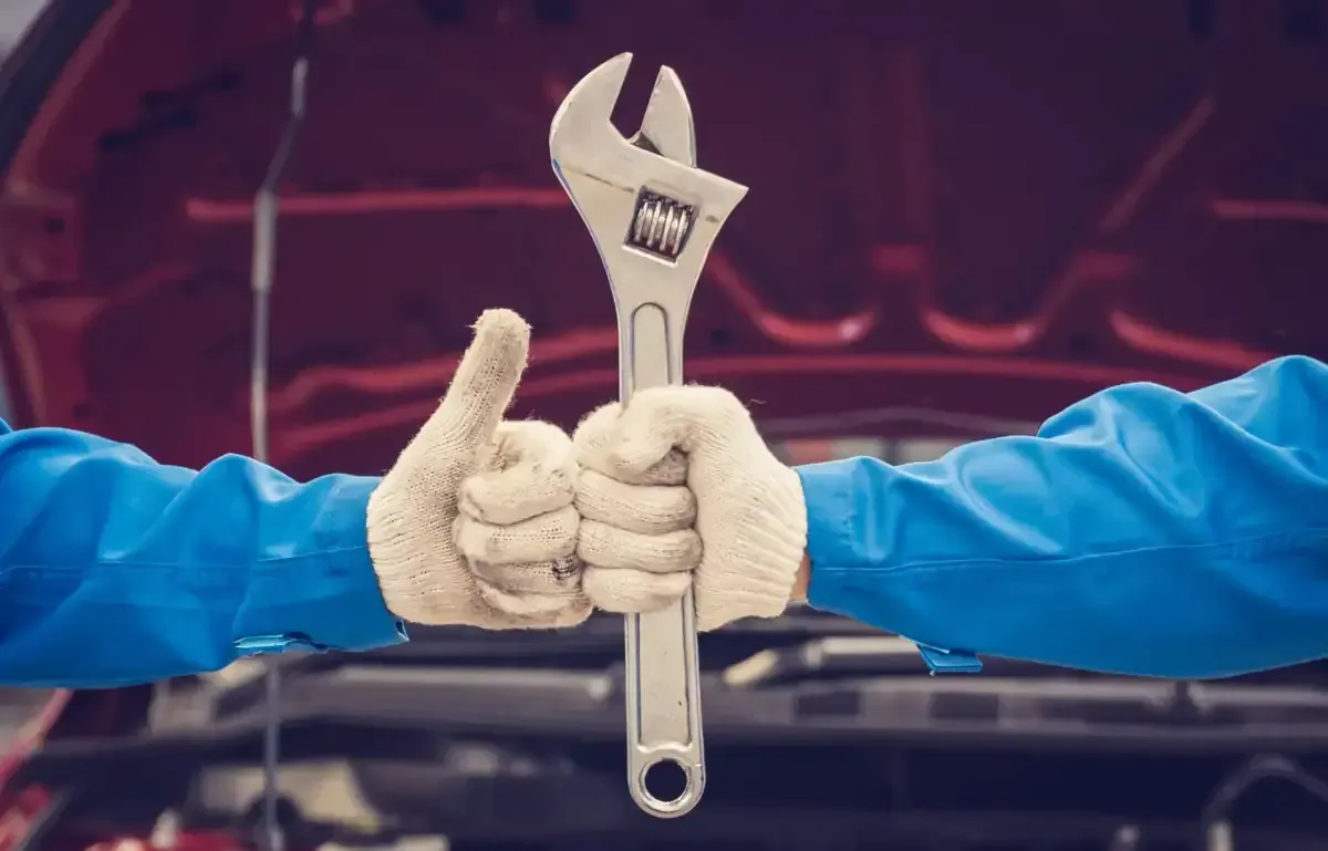 Las manos en guantes de trabajo sostienen una llave inglesa, con los pulgares hacia arriba.