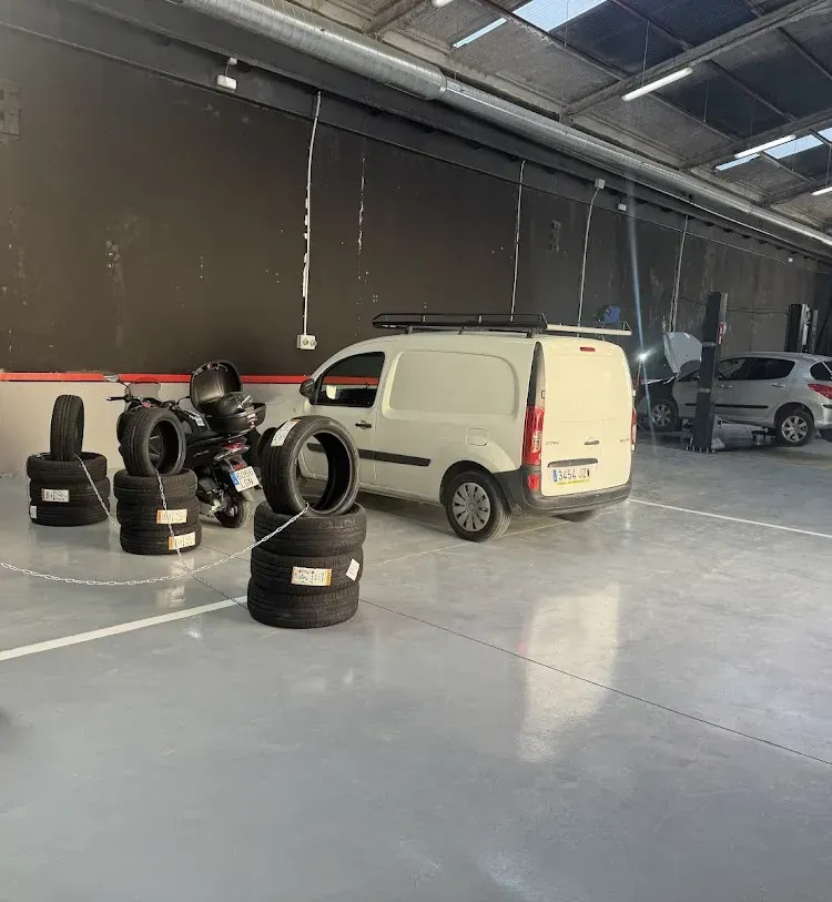 Furgoneta blanca en un entorno de garaje con pilas de neumáticos y una motocicleta.