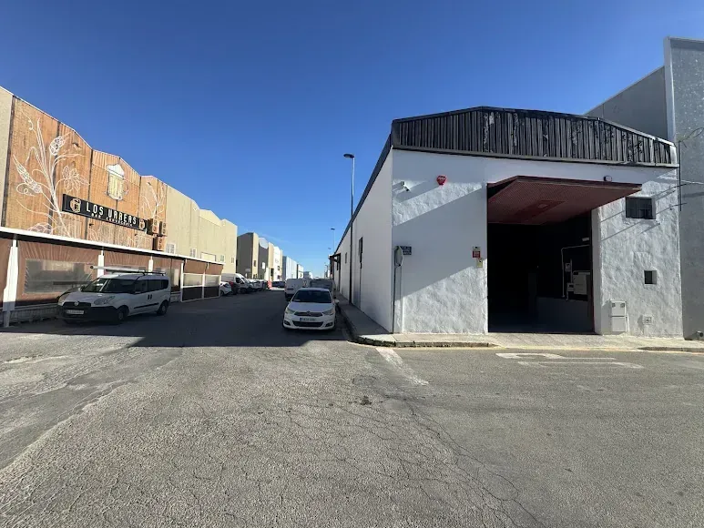 Un edificio blanco con una entrada abierta y una vista de la calle con autos estacionados bajo un cielo azul.