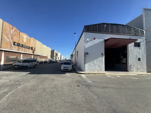 Un edificio blanco con una entrada abierta y una vista de la calle con autos estacionados bajo un cielo azul.
