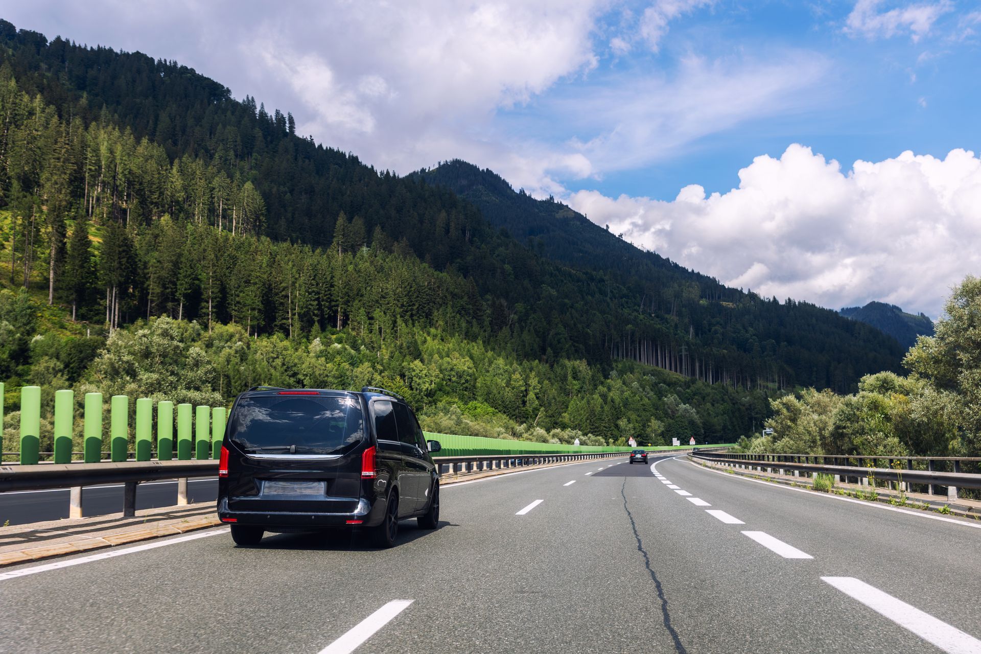 Un SUV noir roule sur une route de montagne sous un ciel d'un bleu éclatant