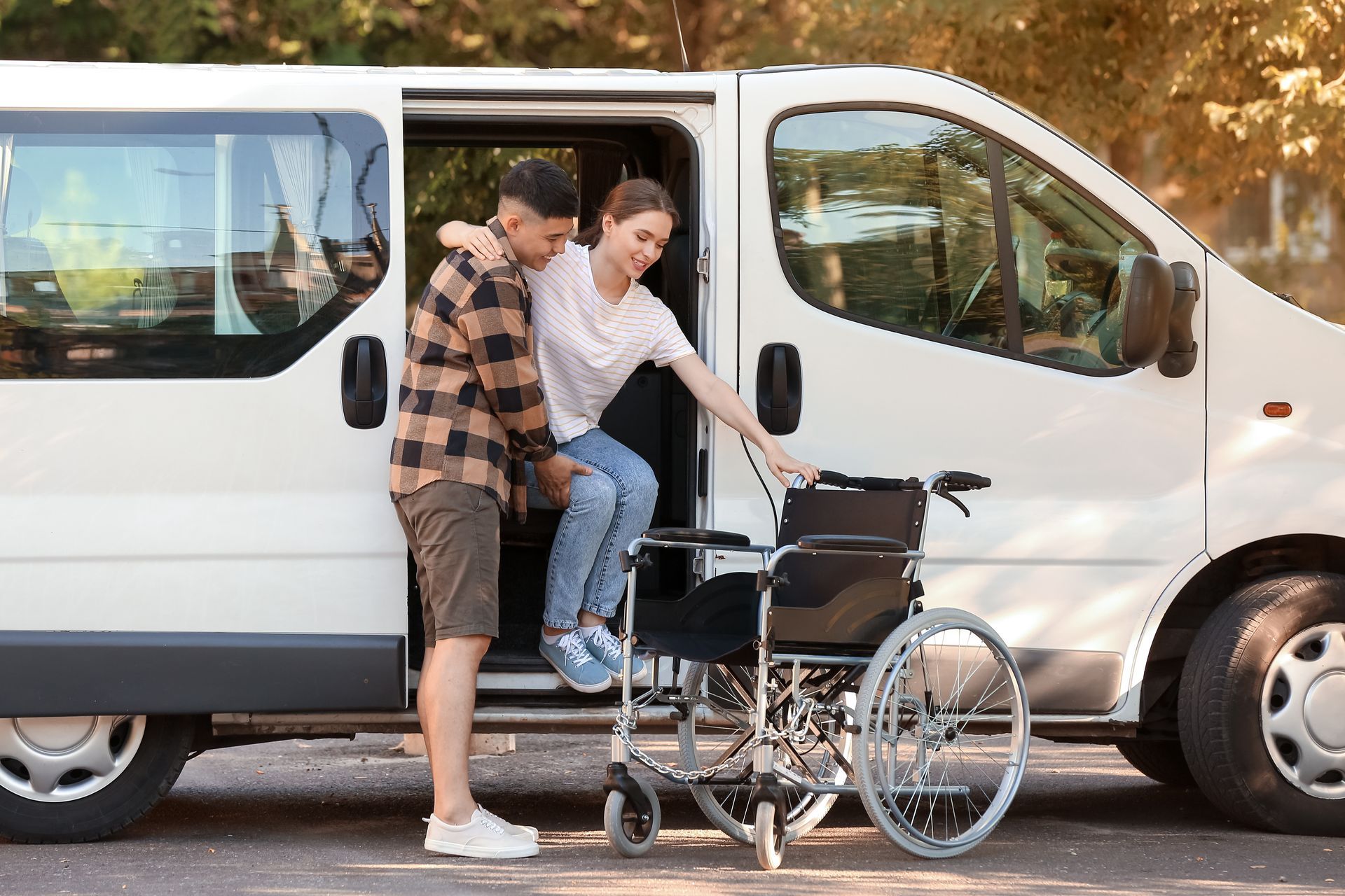 Un homme aide une femme à s'installer dans un fauteuil roulant à côté d'une camionnette blanche dans la rue