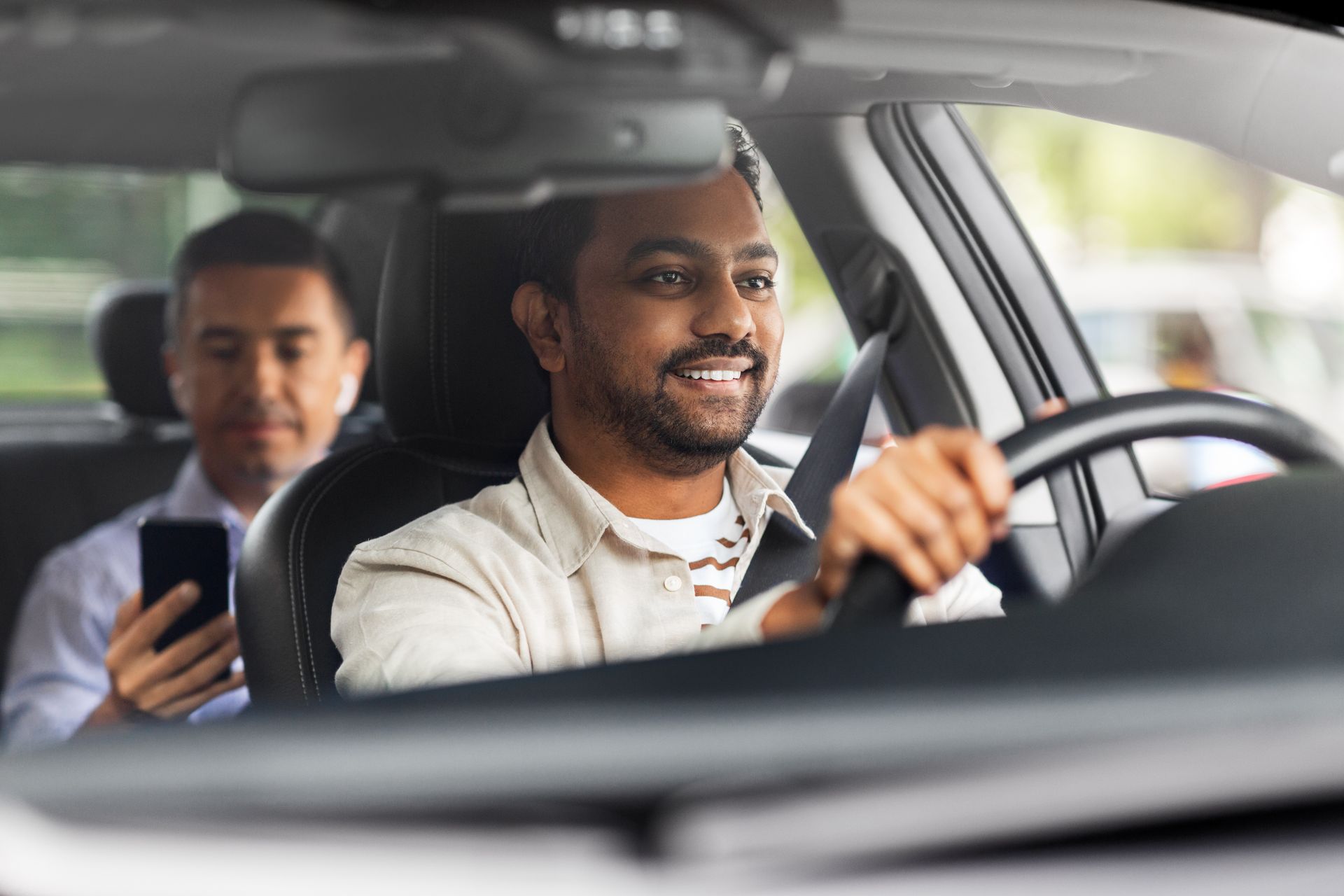 Deux personnes dans une voiture ; le conducteur sourit en conduisant et le passager regarde son téléphone.