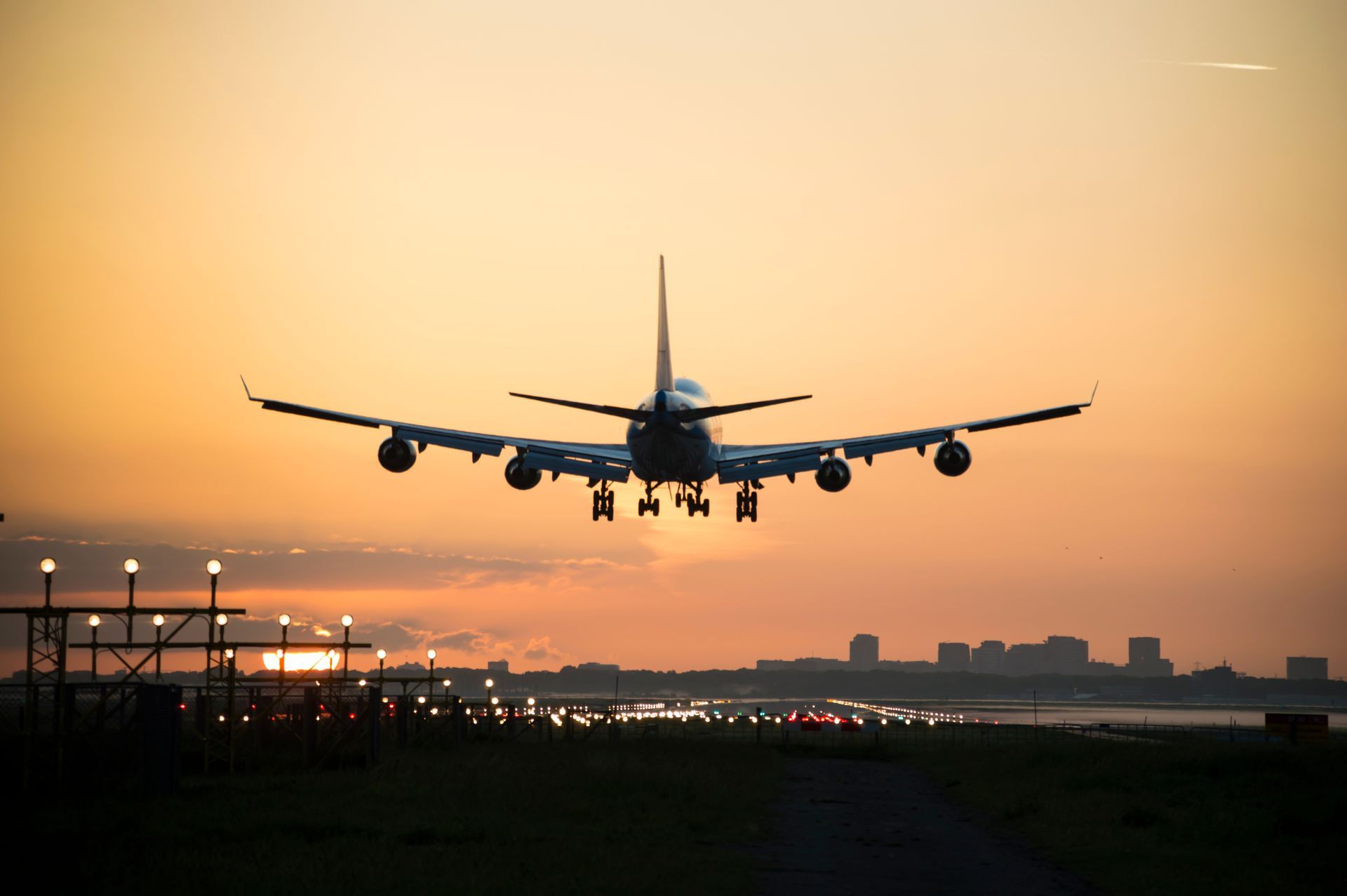 Atterrissage d'un avion au coucher du soleil ; silhouette sur fond de ciel orangé et de silhouette urbaine au loin.