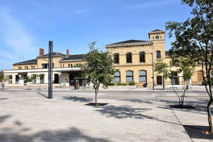 Bâtiment jaune historique avec arches et tour sur une place ensoleillée sous un ciel bleu clair