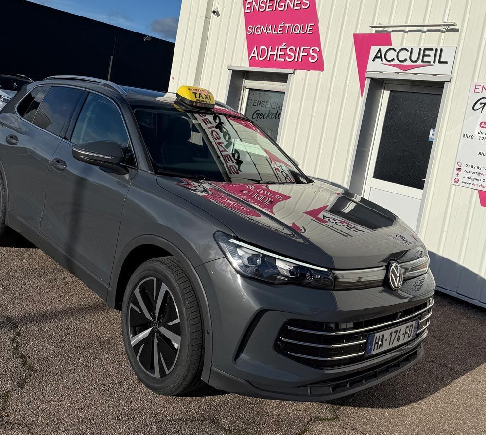 Taxi gris de la marque Volkswagen stationné devant un bâtiment avec enseigne.