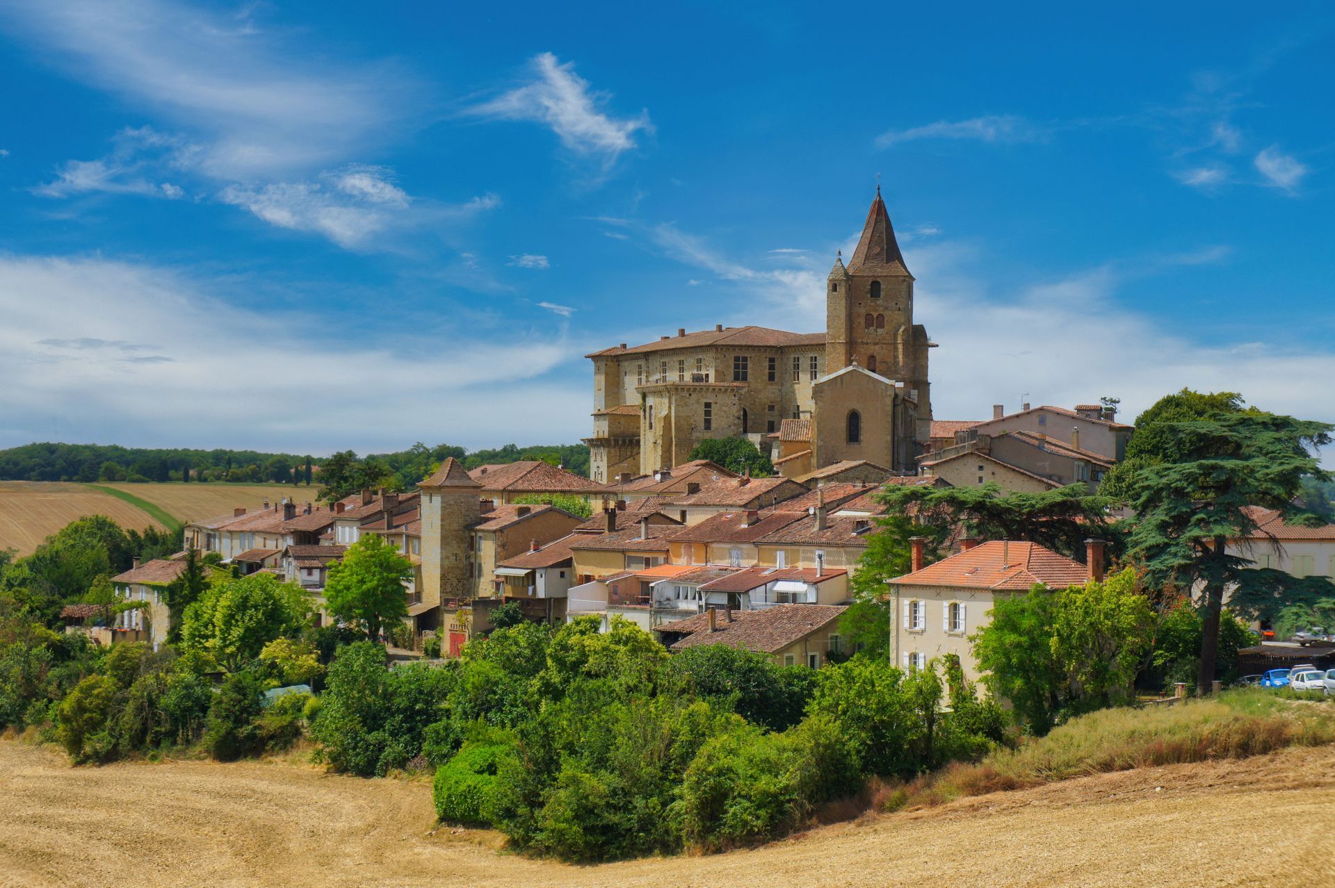 Village perché sur une colline avec un clocher en pierre, des toits de tuiles et des champs sous un ciel bleu