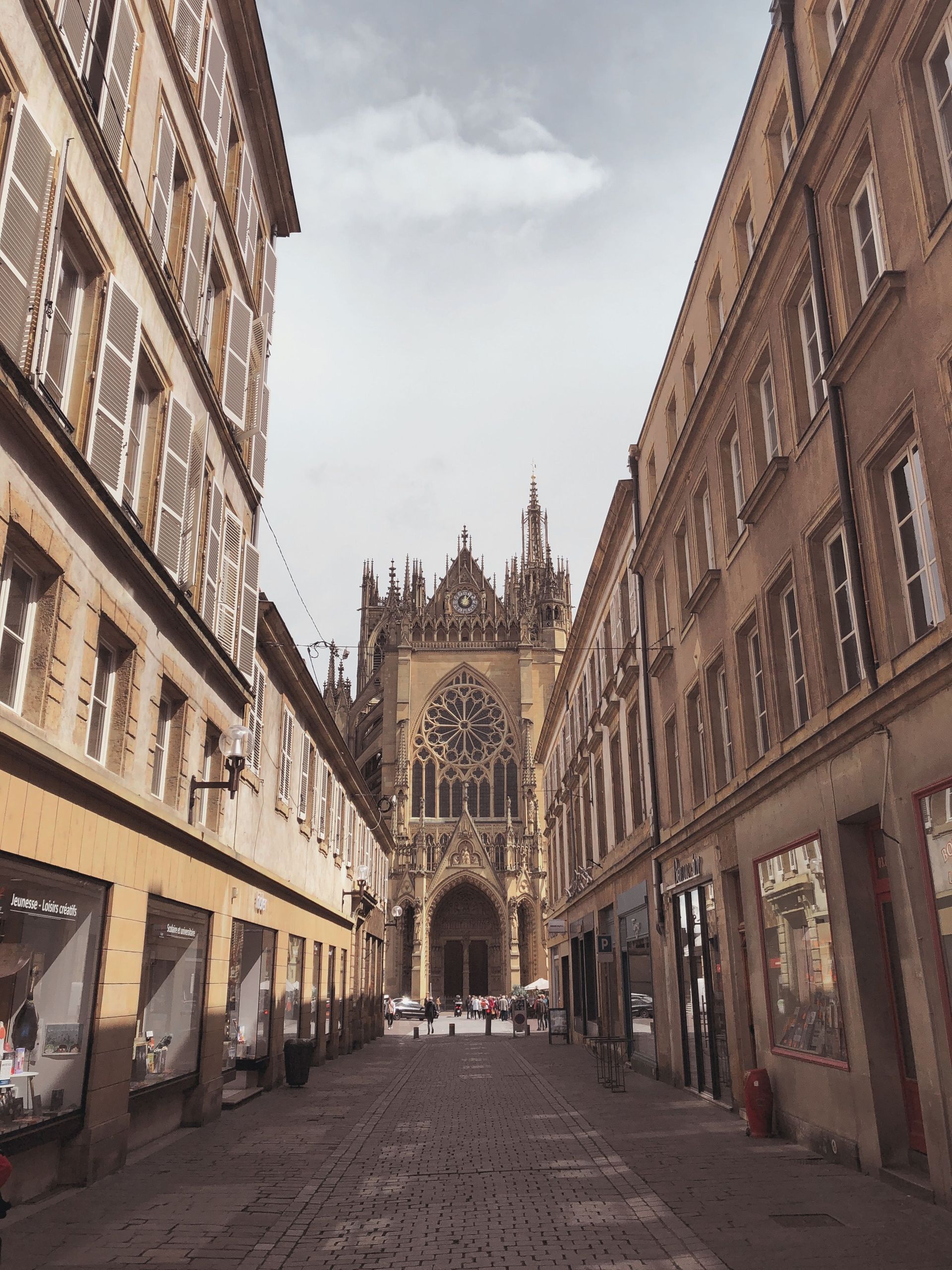 Rue pavée étroite bordée de boutiques, menant à une cathédrale gothique au loin.