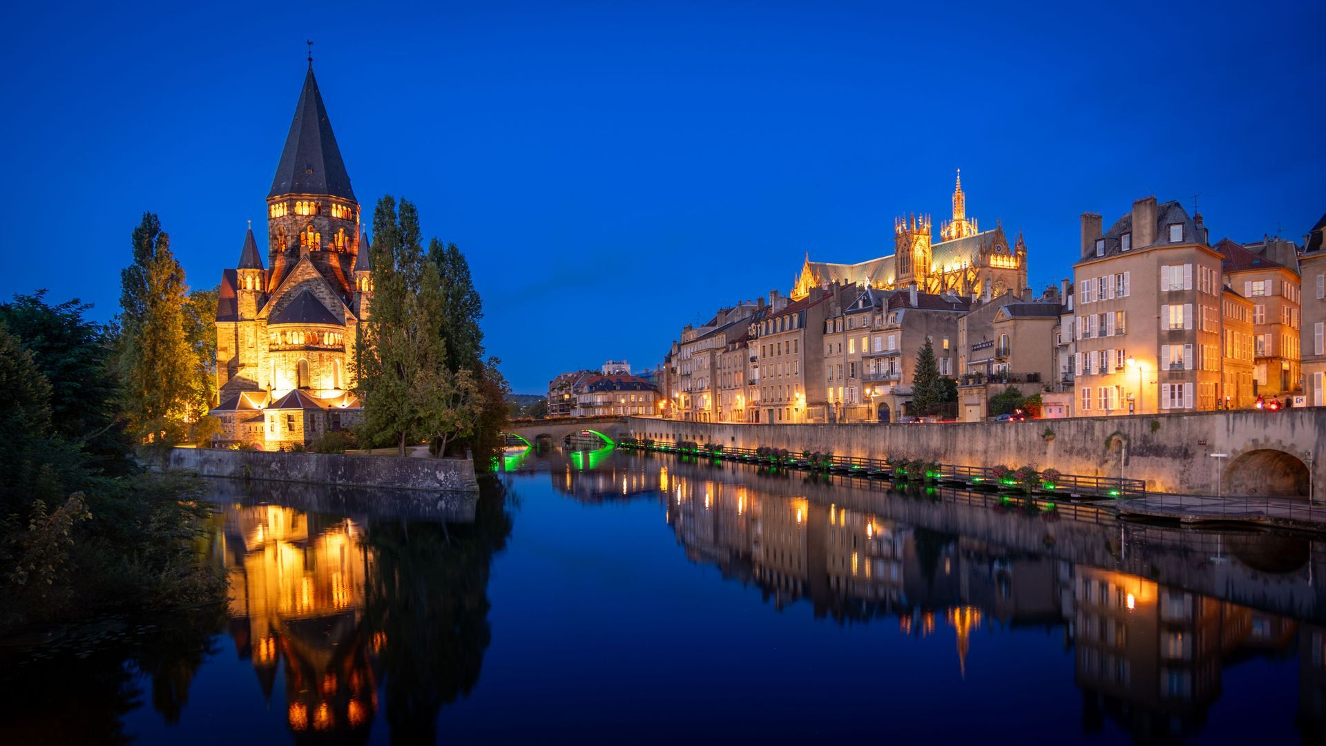 Vue crépusculaire d'une ville riveraine avec ses bâtiments historiques illuminés et leurs reflets sur l'eau calme