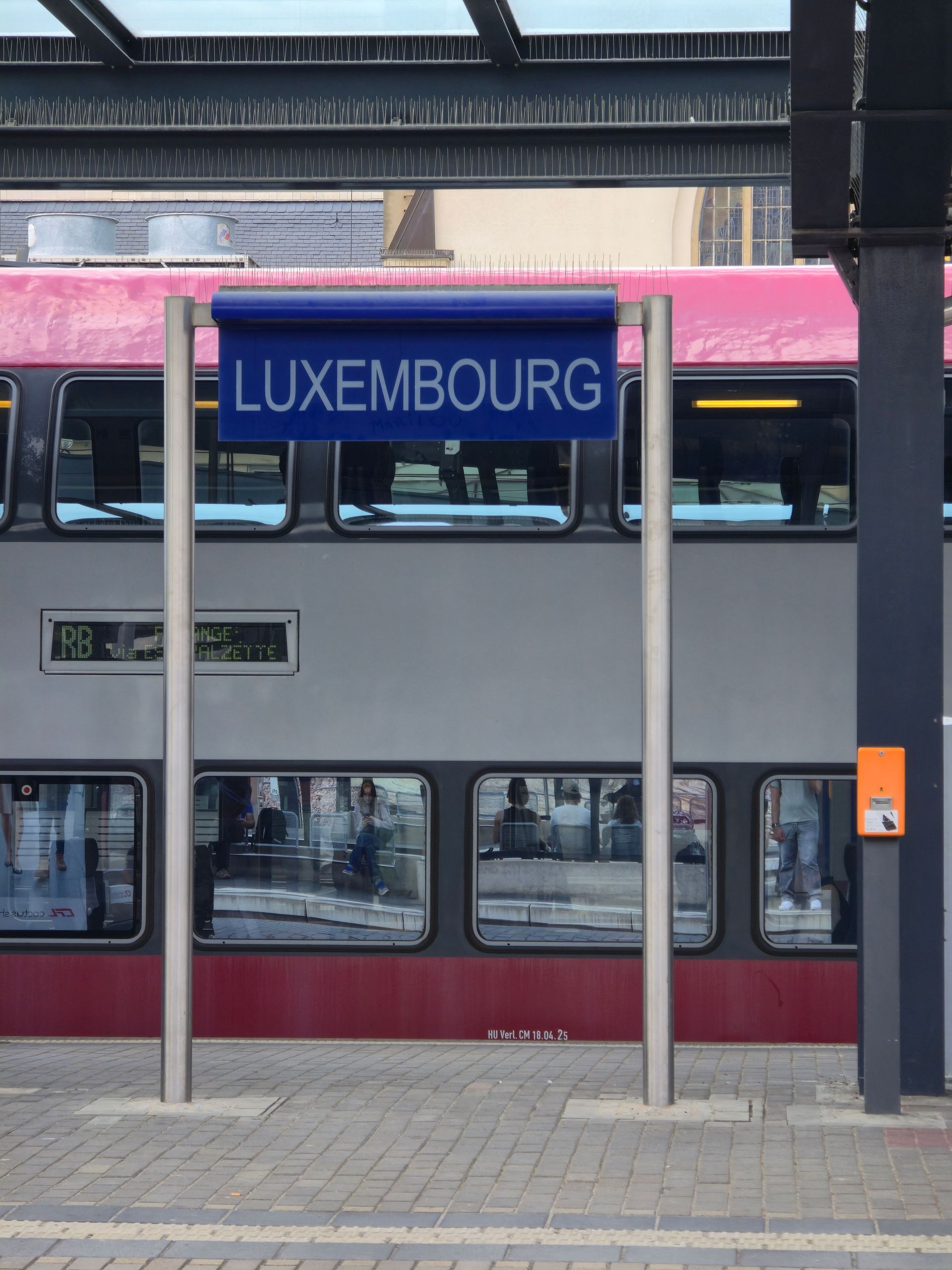 Panneau bleu de la gare de Luxembourg avec un train en arrière-plan sur le quai
