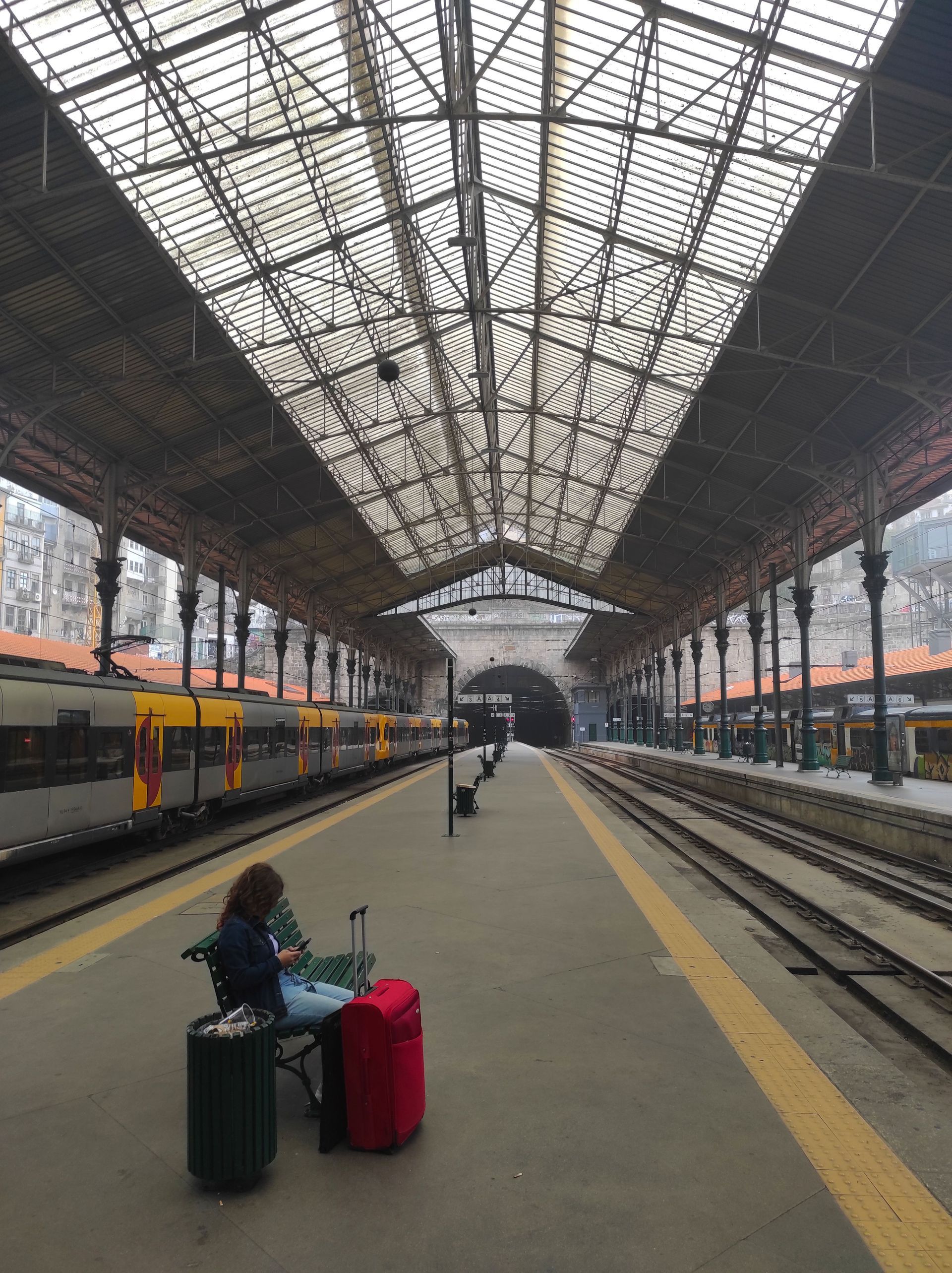 Quai de gare avec un voyageur assis et des bagages rouges sous une grande verrière