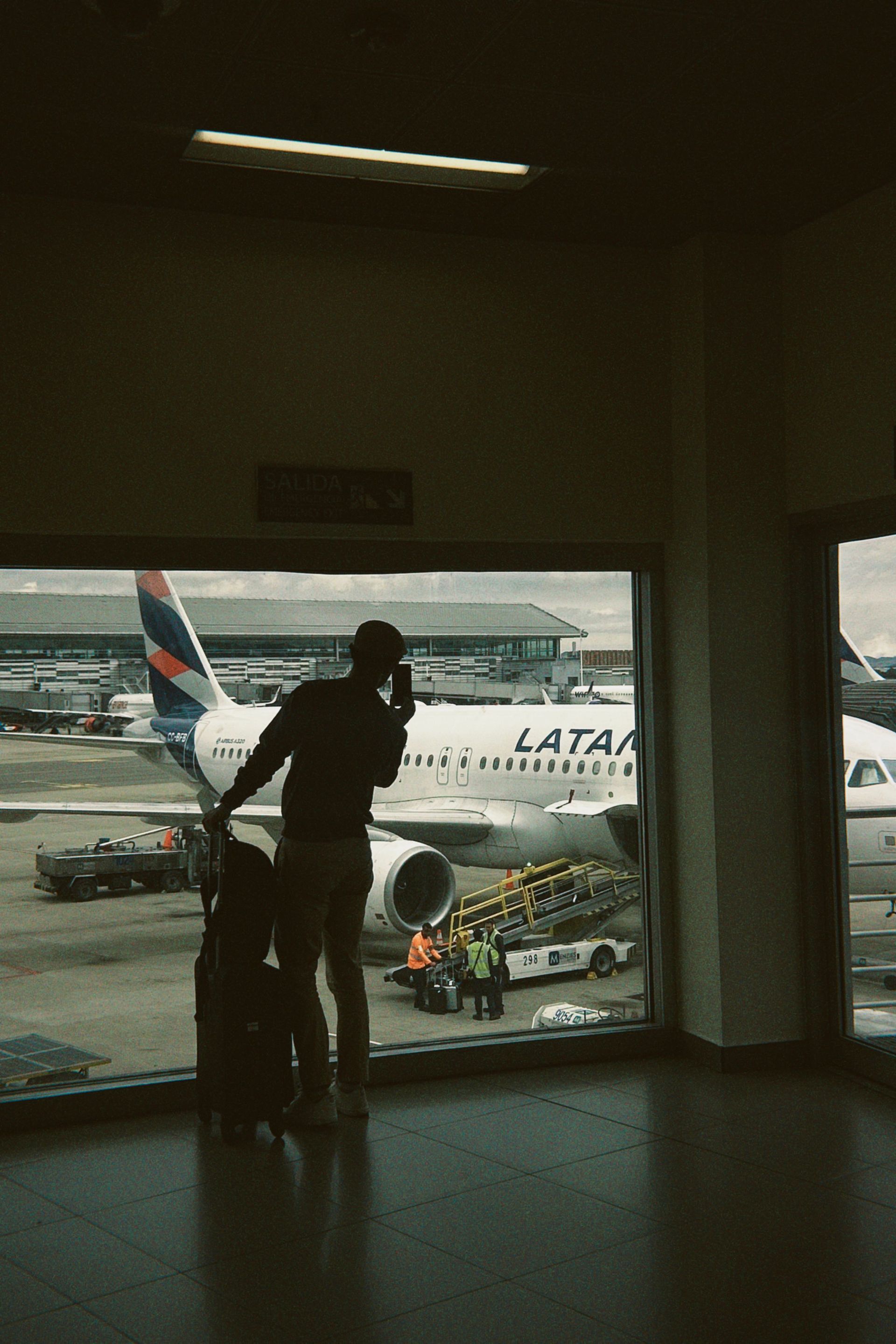 Voyageur en silhouette regardant un avion de LATAM à travers une vitre d'aéroport