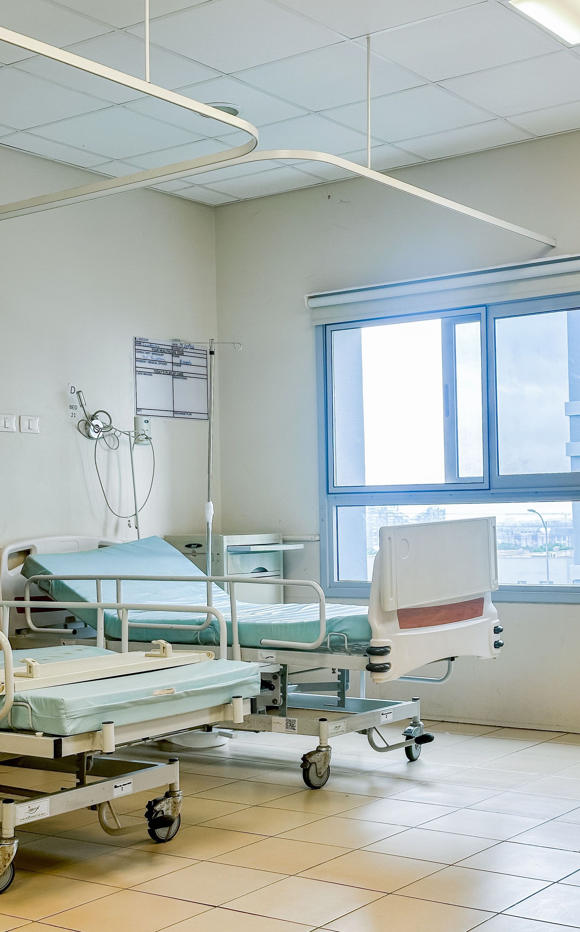 Chambre d'hôpital vide avec des lits, du matériel médical et une grande fenêtre avec des rideaux bleus.