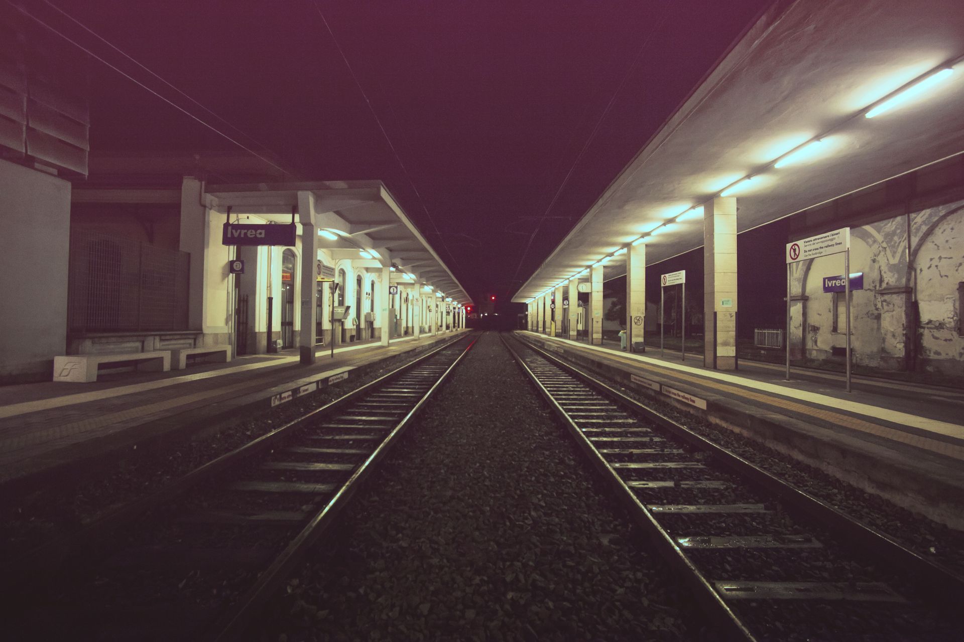 Quai de gare désert la nuit, les voies s'estompant au loin sous les projecteurs.